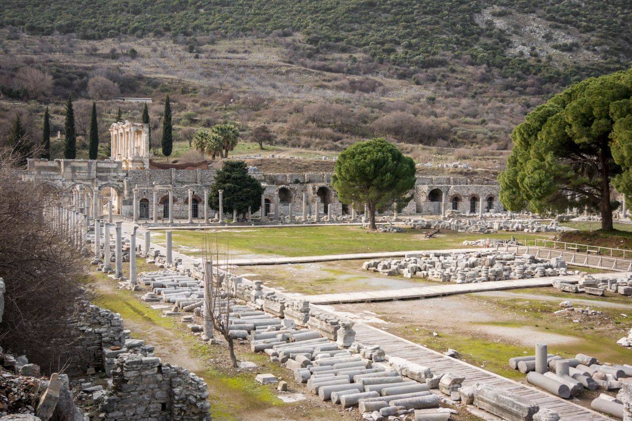 An open excavated area at Ephesus with rows of fallen columns and the Library of Celsus beyond.