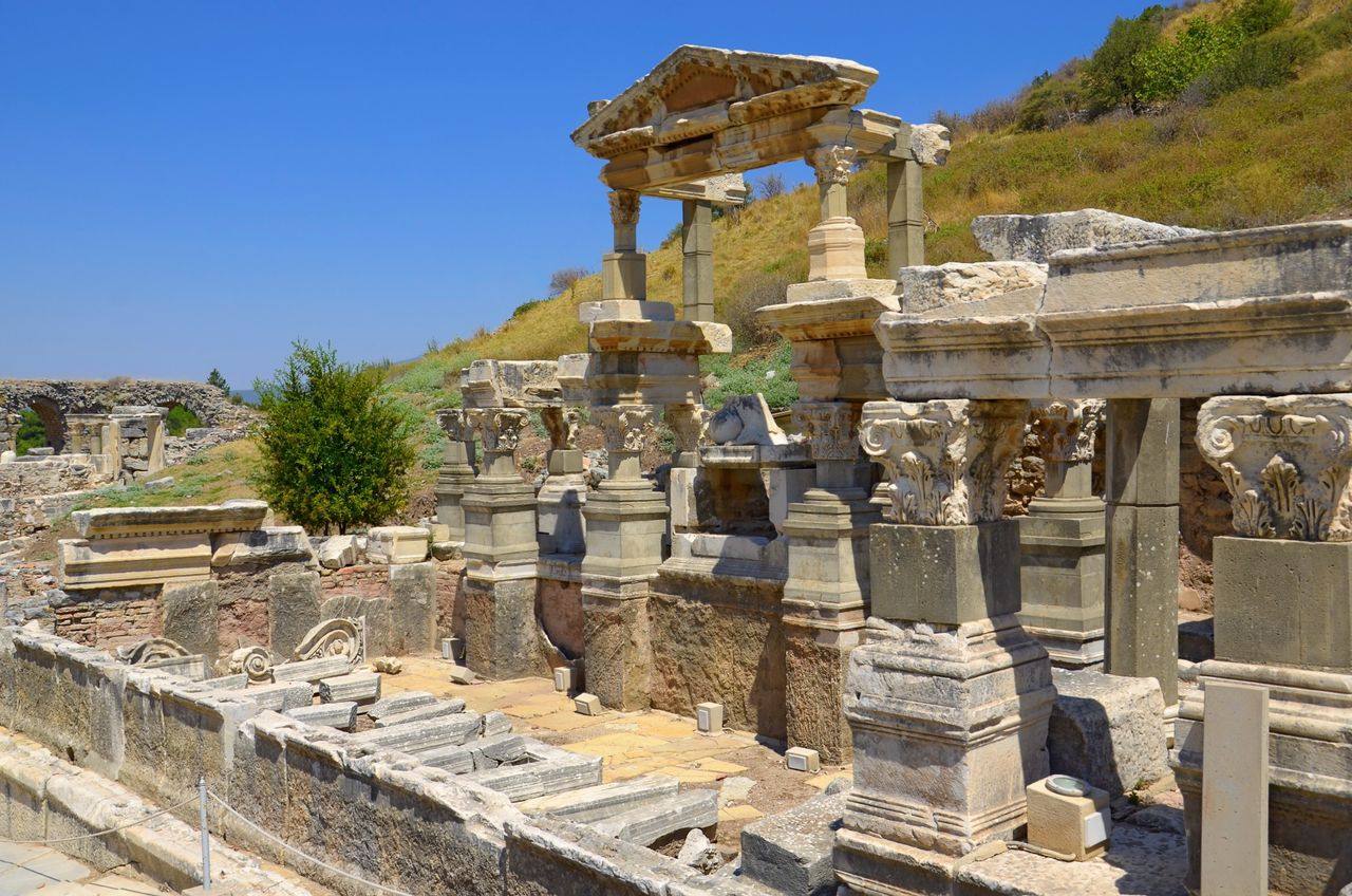 A restored monumental fountain building at Ephesus with carved Corinthian capitals and re-erected columns on a hillside.