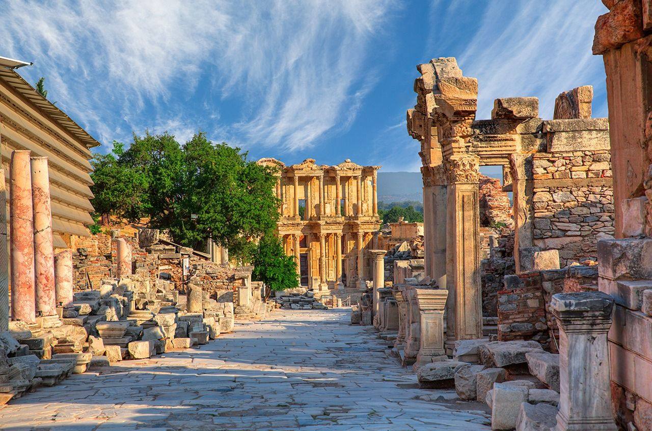 A paved ancient street at Ephesus lined with column fragments, leading toward the Library of Celsus.