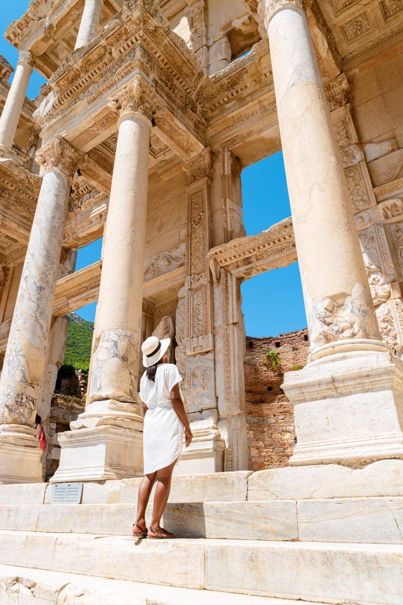 A visitor in a sun hat standing on the steps in front of the Library of Celsus.
